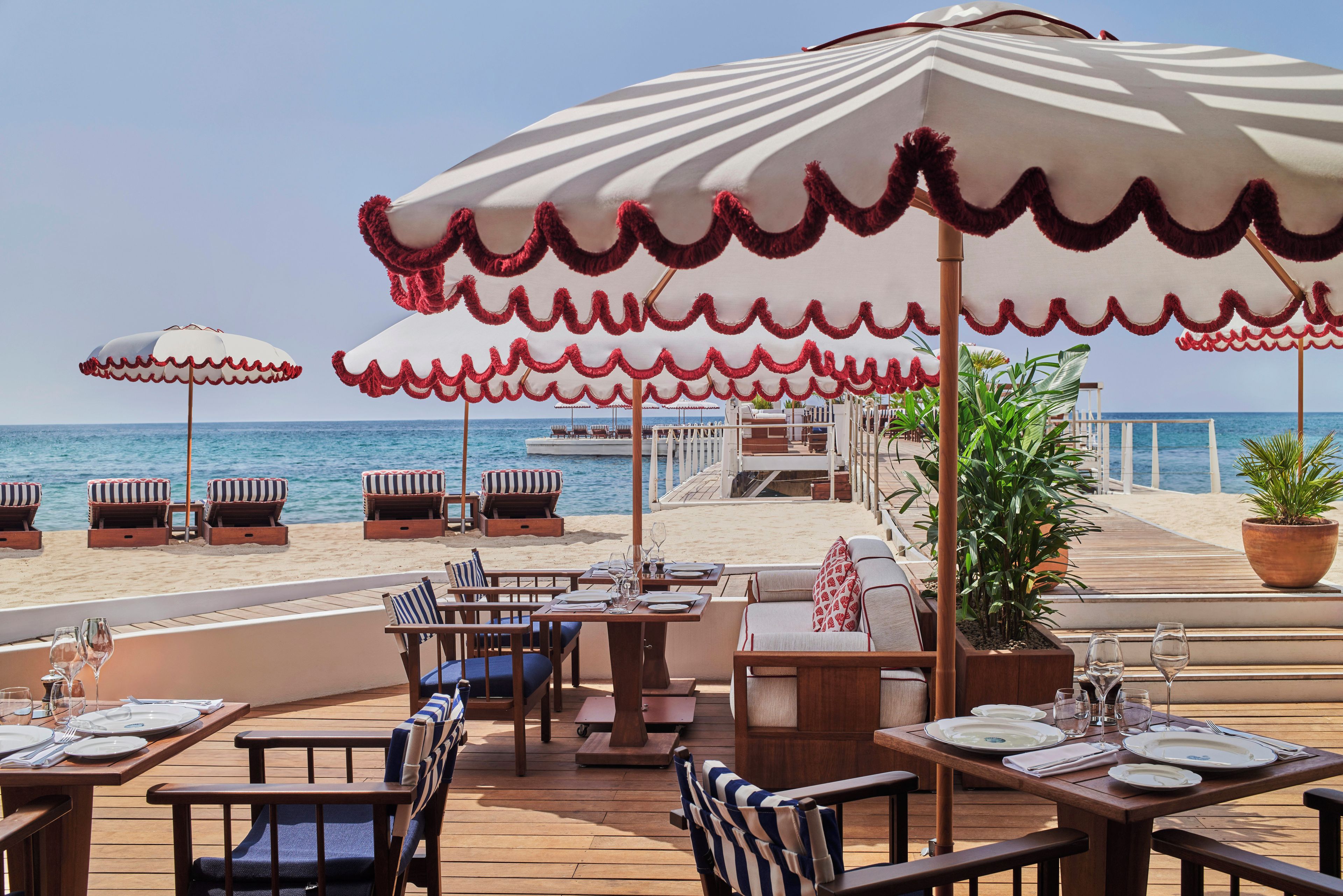 A beachfront restaurant with outdoor seating, umbrellas, and a view of the sea.