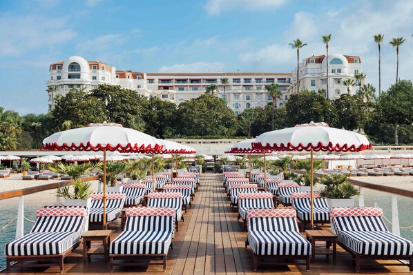 A poolside area with lounge chairs and umbrellas, a pool, and a hotel building in the background.