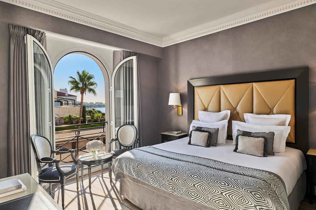 Habitación de hotel con una cama grande, un balcón con vistas y una zona de estar con una mesa y sillas.