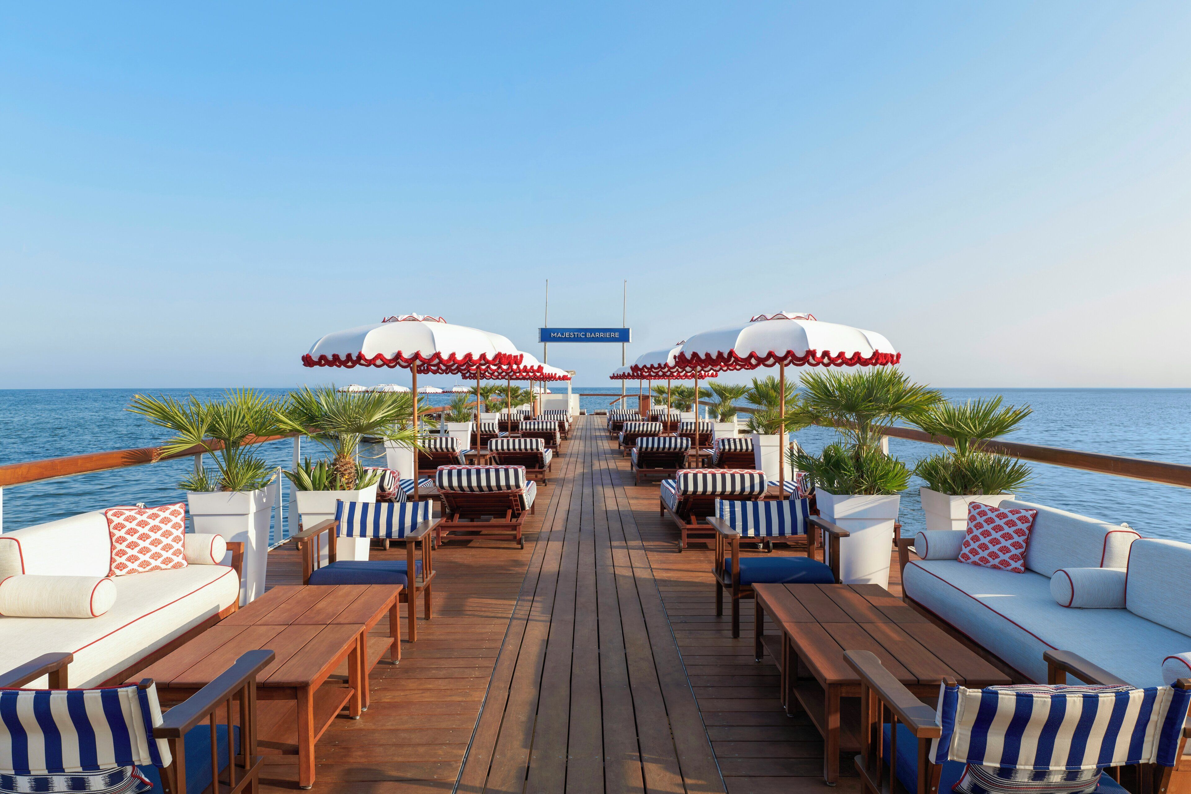 A deck with wooden furniture, white cushioned sofas, striped chairs, and umbrellas.