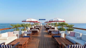 A deck with wooden furniture, white cushioned sofas, striped chairs, and umbrellas.