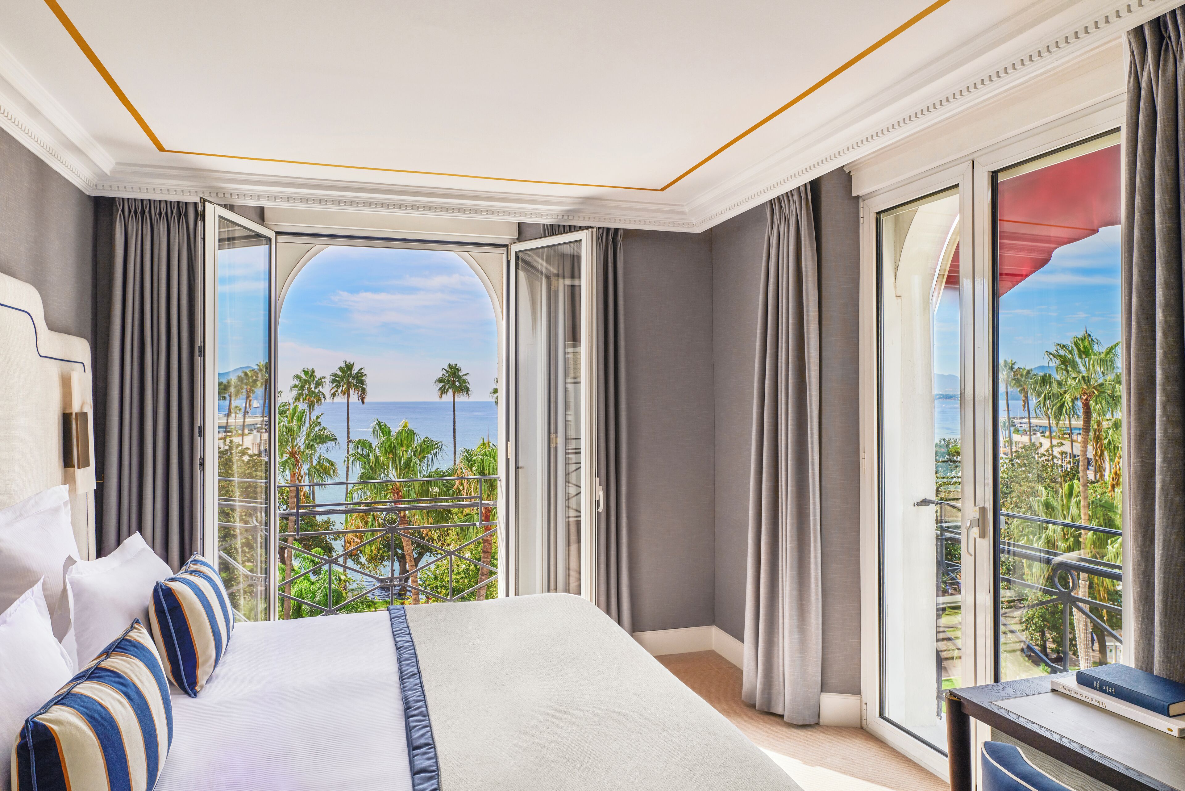Une chambre d’hôtel avec un grand lit, une vue sur les palmiers et l’océan, et un balcon doté d’une balustrade.