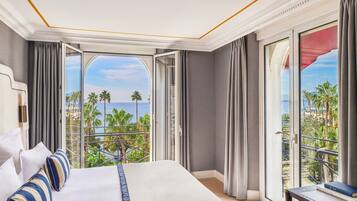 A hotel room with a large bed, a desk, and a view of palm trees and the ocean.