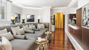 A modern living room with a grey sofa, two side tables with lamps, and a wooden coffee table with a teapot and fruit.