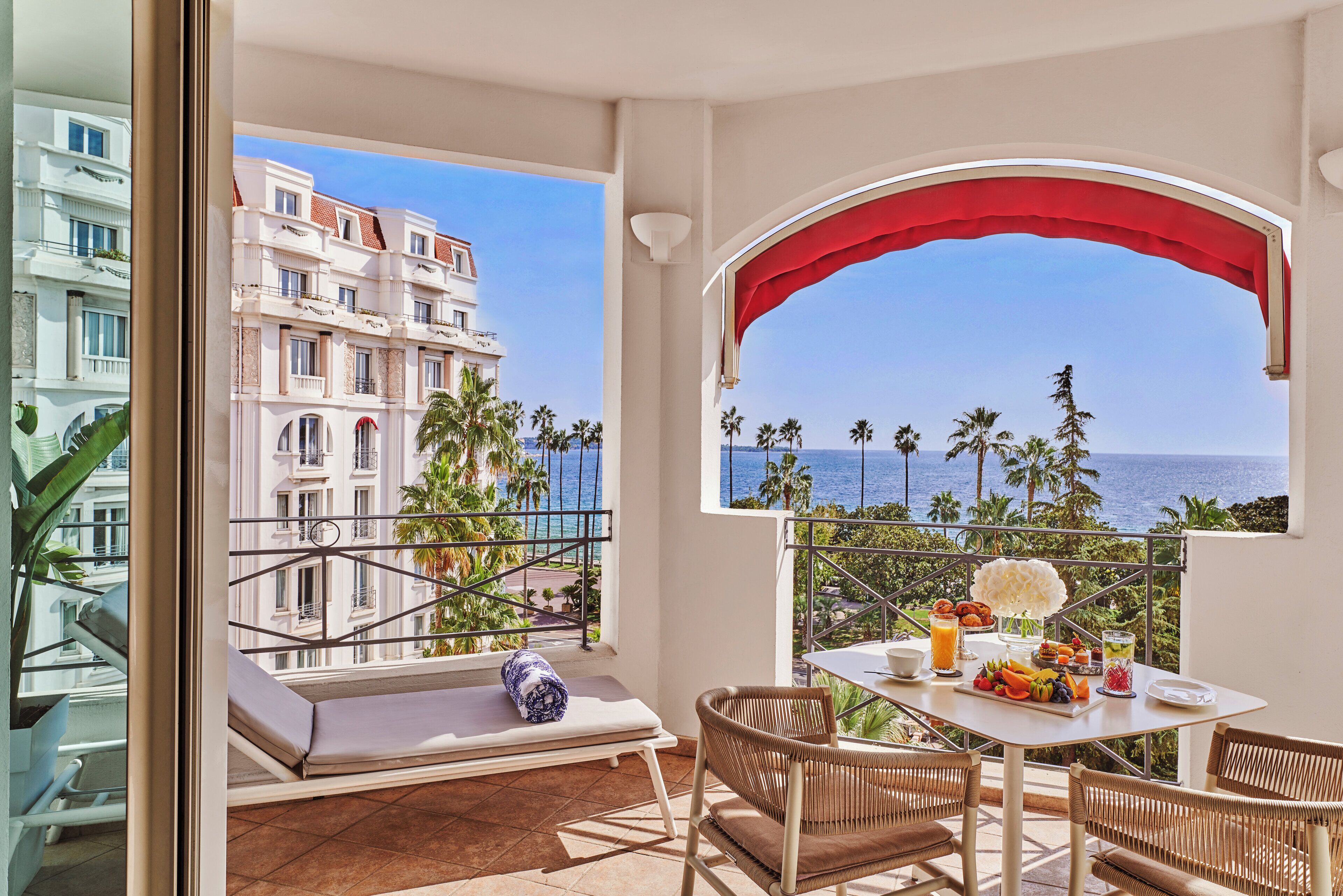 Un balcon avec vue sur la mer, une table à manger où le petit-déjeuner est servi, et un coin salon avec un coussin.