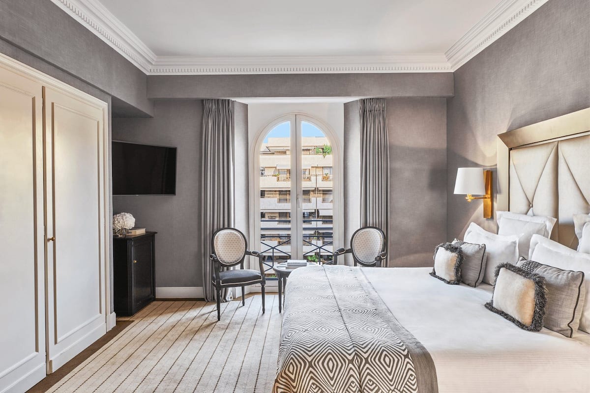 Una habitación de hotel con una cama grande, dos sillas, una mesita y un televisor.