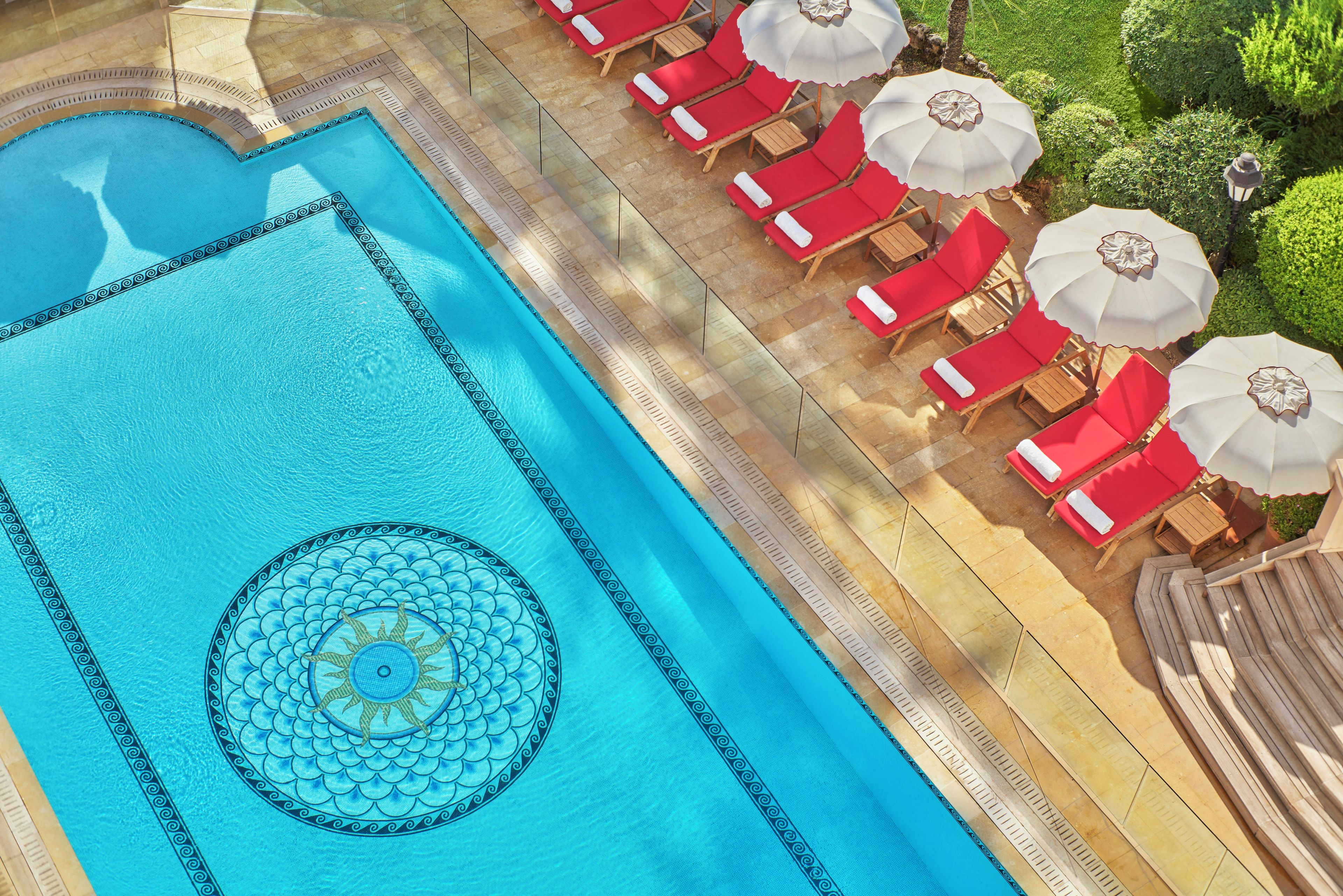 Una piscina con un diseño decorativo, rodeada de tumbonas y sombrillas.