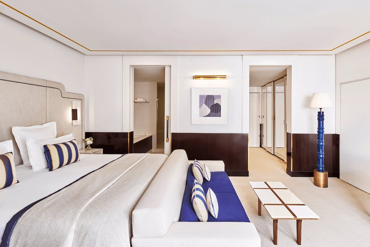 Habitación de hotel con una cama grande, un sofá, una mesita de noche, una lámpara y un cuadro en la pared.
