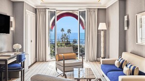 Una habitación de hotel con balcón, un sofá, una silla, una mesa y un televisor.
