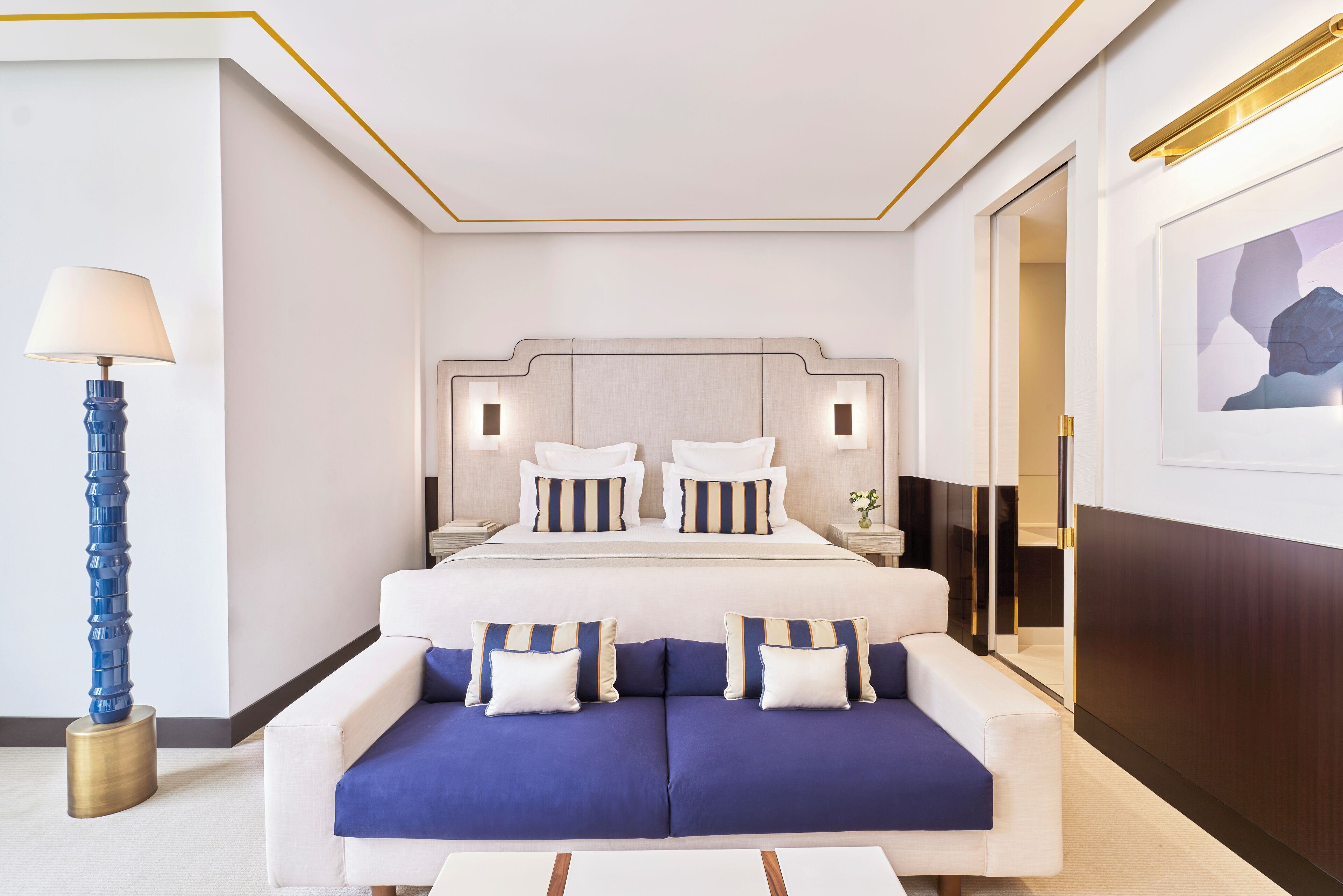A modern hotel room with a large bed, a sofa, a lamp, and a painting on the wall.