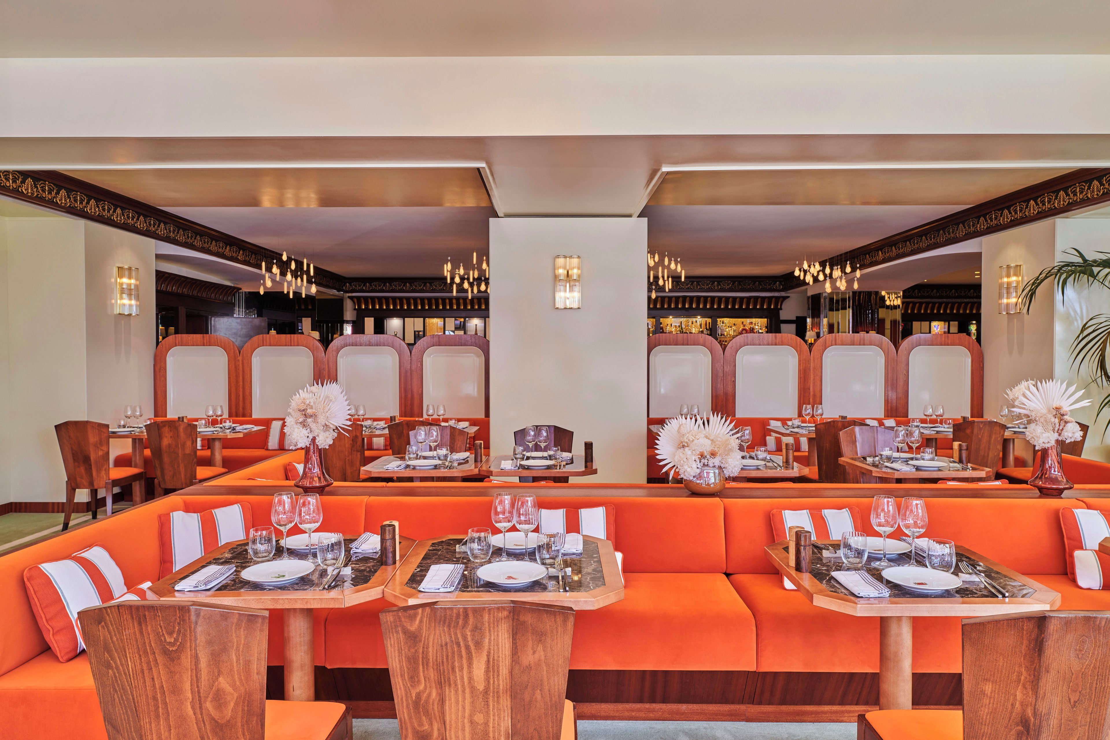 A restaurant with orange seating, wooden tables, and hanging light fixtures.