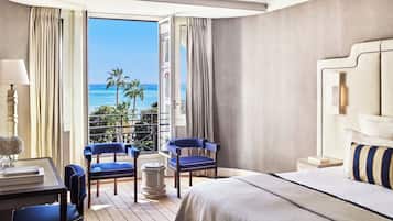 Habitación de hotel con una cama grande, dos sillas azules, una mesita y vista al océano.