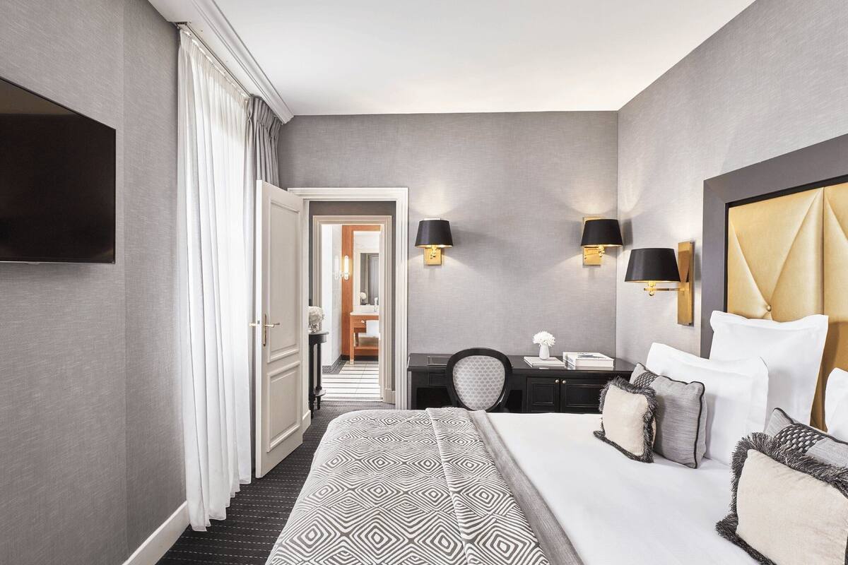 Habitación de hotel con una cama grande, un escritorio con silla, un televisor de pantalla plana en la pared y dos lámparas de pared.