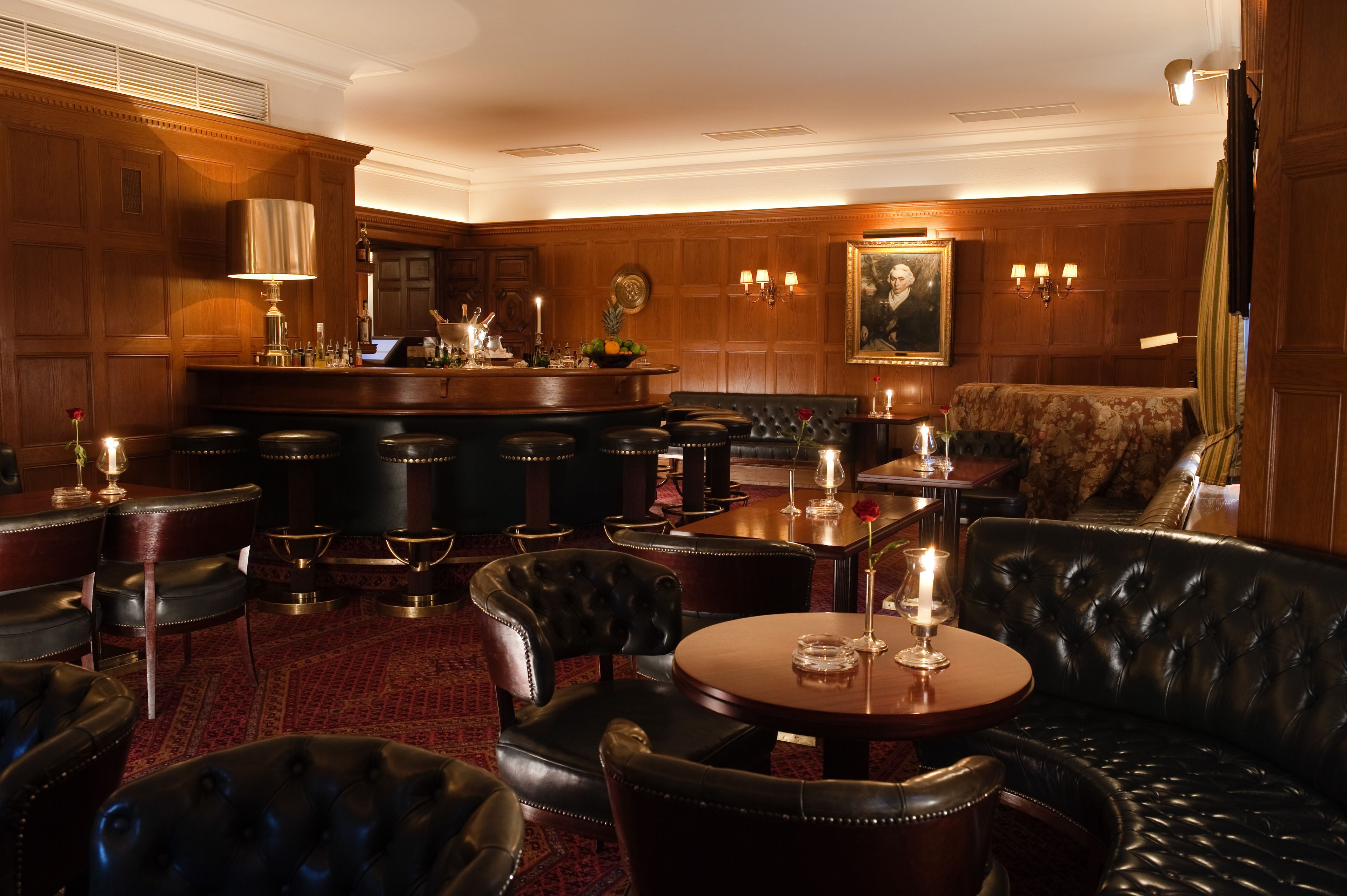 A classic bar area with leather seating, a bar counter, and a large painting on the wall.