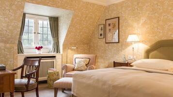 Een slaapkamer met een bed, een stoel, een bureau, een raam met gordijnen en een radiator.