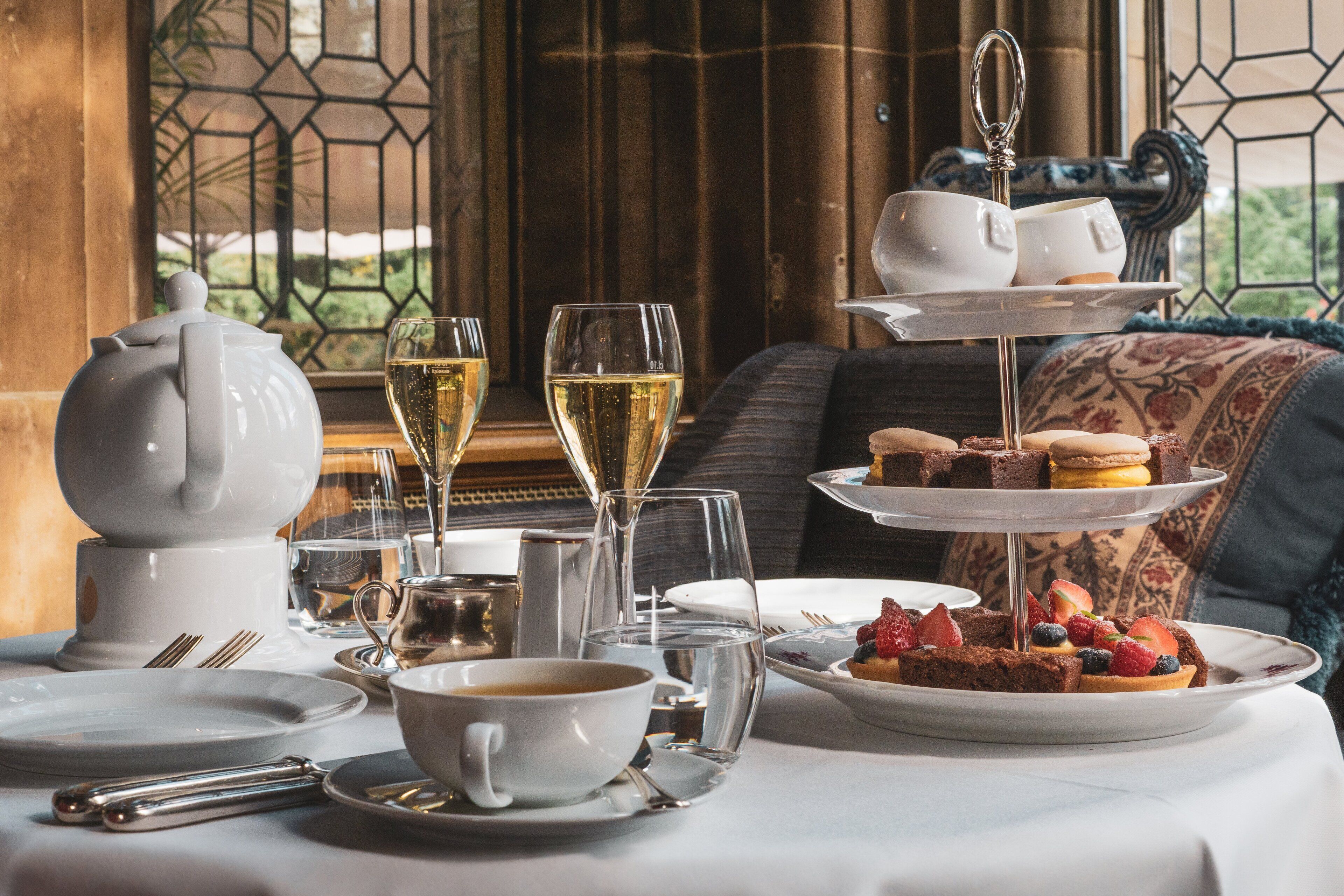 Une table dressée avec une théière, des tasses, des verres et un présentoir à gâteaux à plusieurs niveaux, garni de pâtisseries et de fruits.