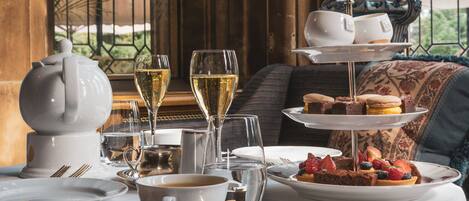 Une table dressée avec une théière, des tasses, des verres et un présentoir à gâteaux à plusieurs niveaux, garni de pâtisseries et de fruits.