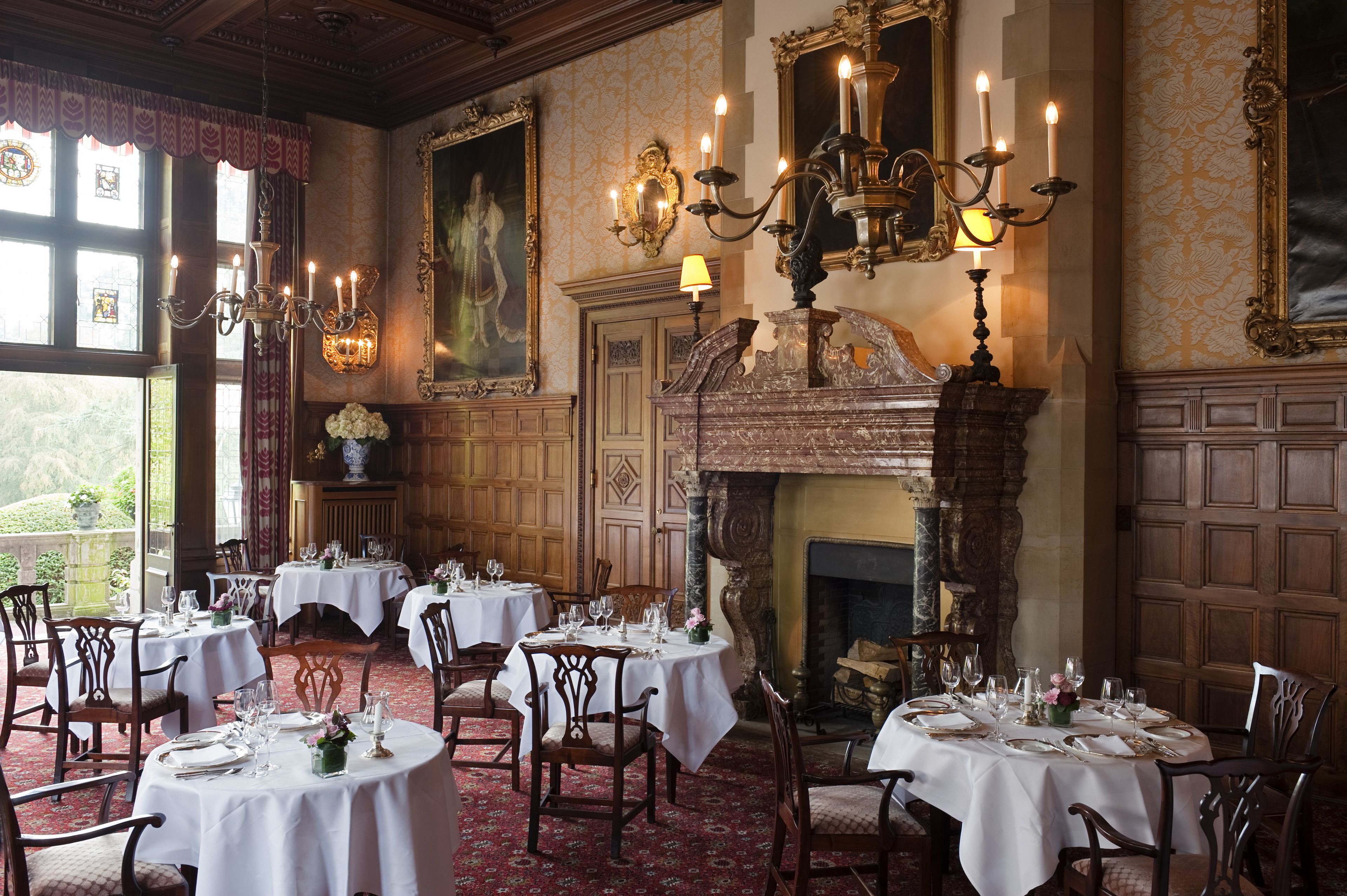 Un comedor con varias mesas dispuestas para una comida, una chimenea y decoraciones ornamentales en las paredes.