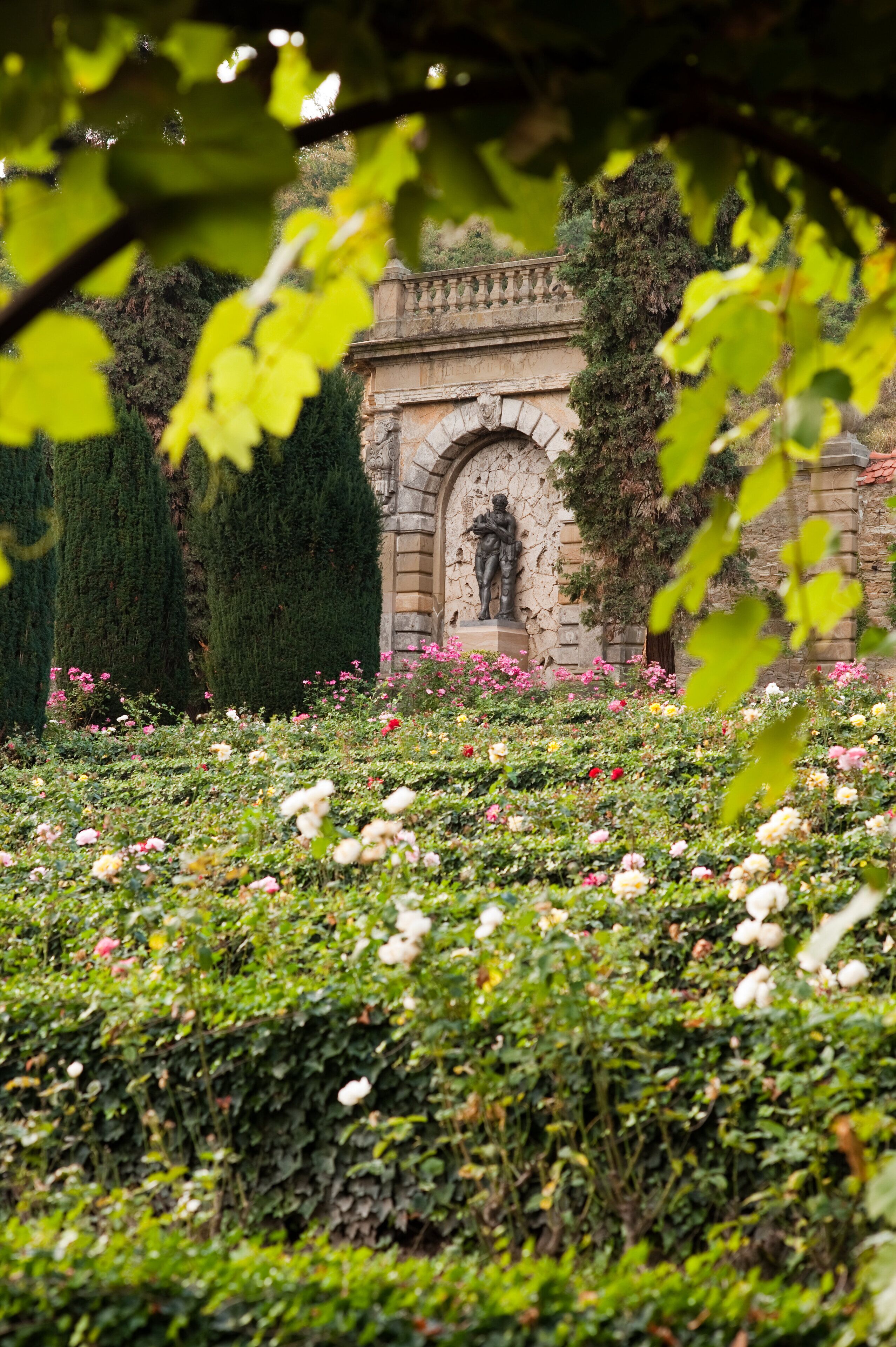 A garden with a statue, stone archway, and lush greenery.