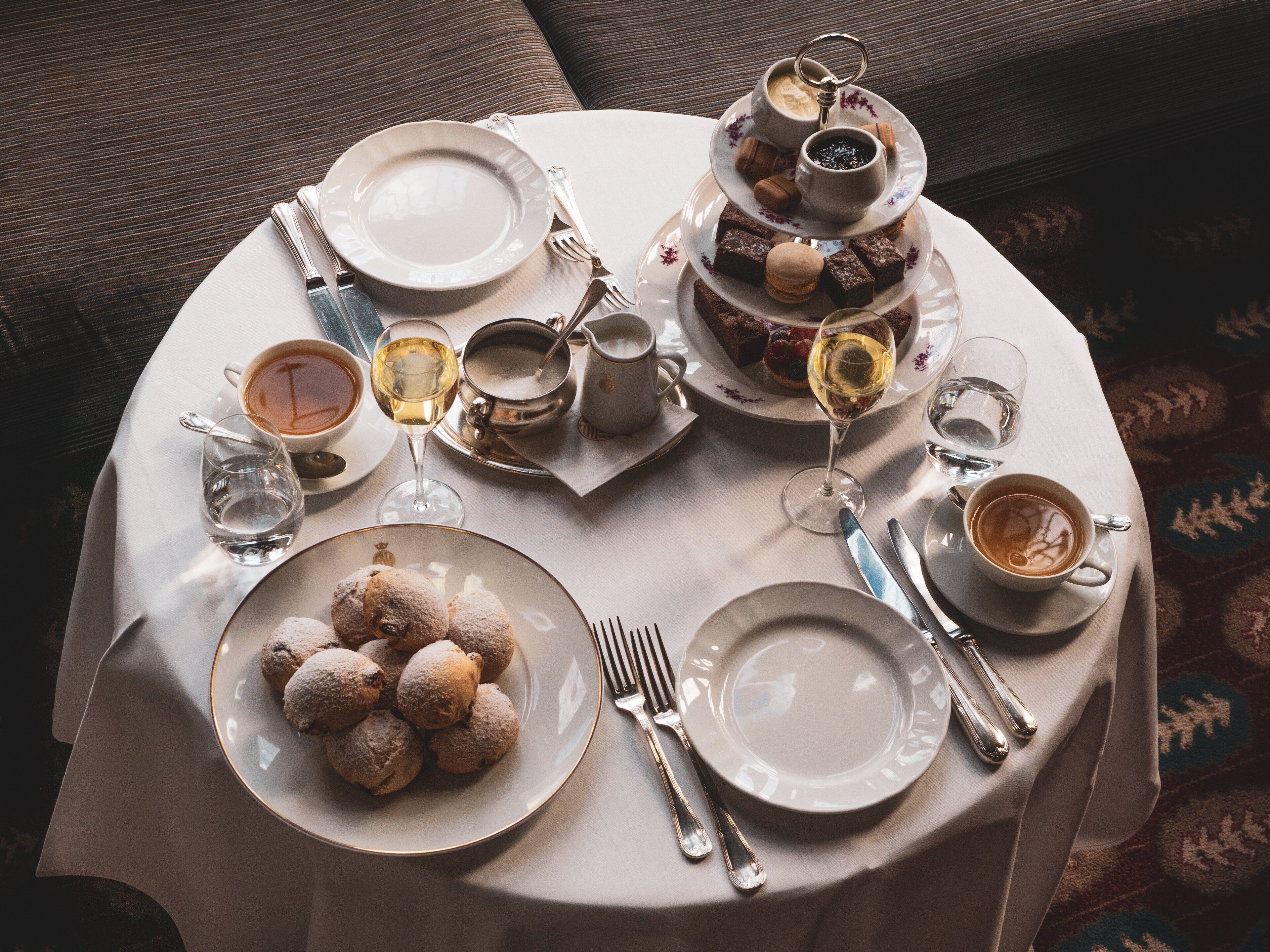 Une table ronde dressée avec des assiettes, des couverts, des verres et un présentoir à gâteaux à plusieurs niveaux.