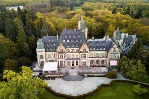 Un edificio grande e histórico con varias secciones y un patio central, rodeado de un bosque frondoso.