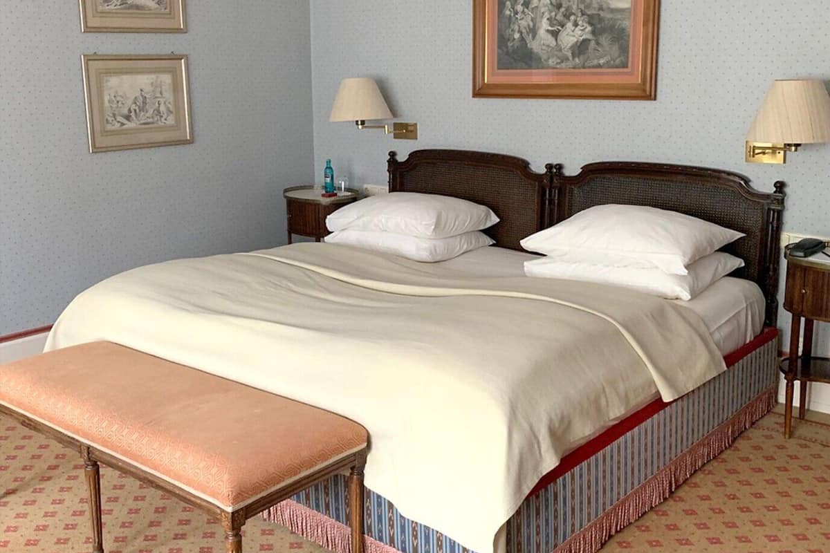 Una cama bien hecha con cabecera de madera, una mesita de noche con lámpara y un banco al pie de la cama.