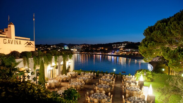 A waterfront restaurant with outdoor seating overlooking a body of water, a flag, and a building labeled "GAVINA".
