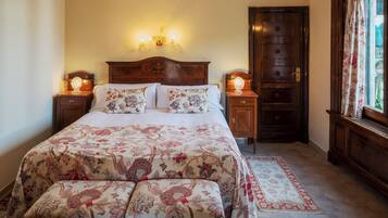 Une chambre avec un grand lit, un ventilateur de plafond, deux tables de chevet avec des lampes, une porte en bois et une fenêtre avec des rideaux.