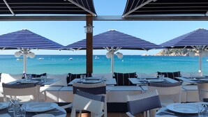 An outdoor dining area with tables and chairs, umbrellas, and a view of the sea.