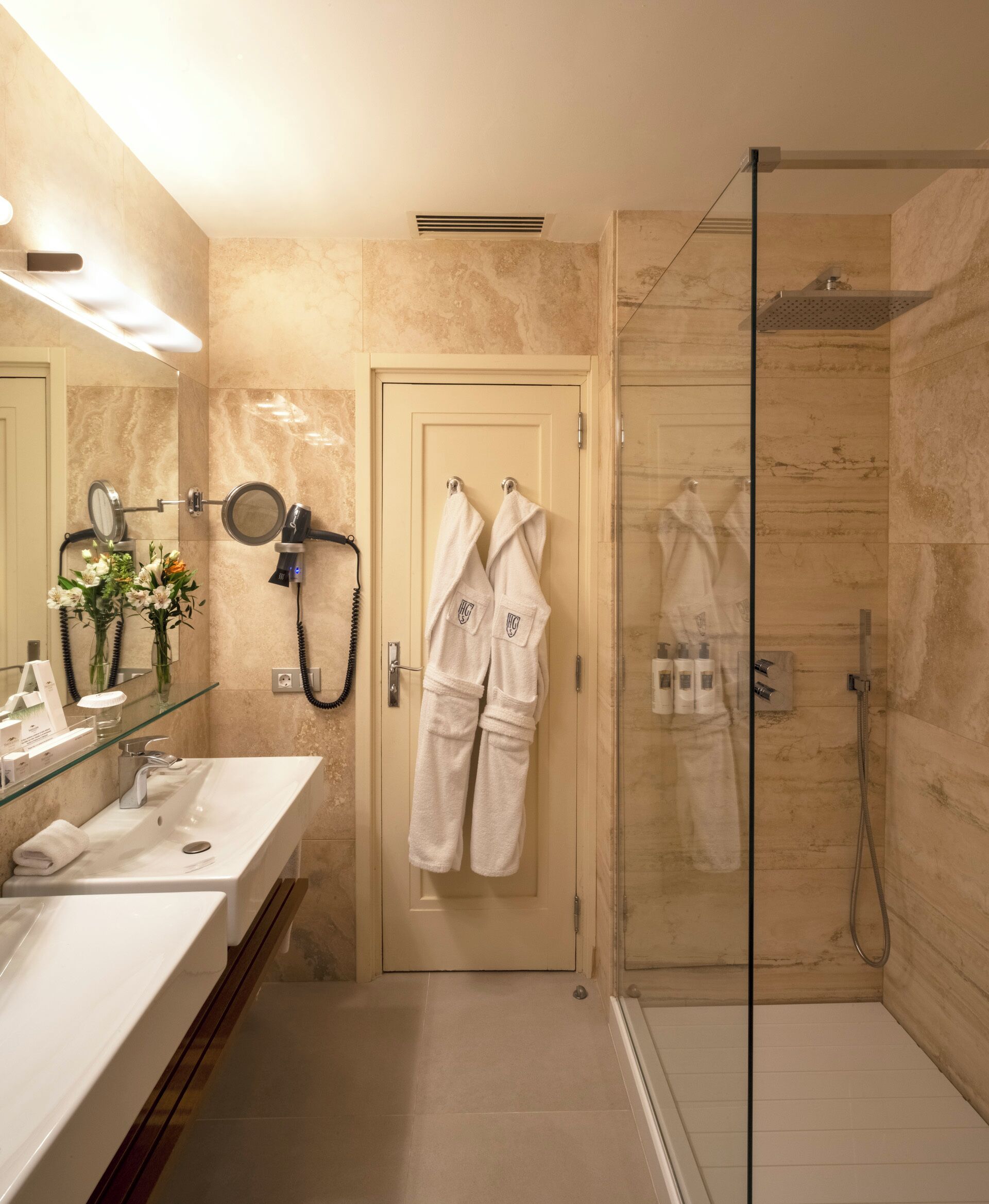 A modern bathroom with a glass shower enclosure, a double sink vanity, and a towel rack with robes.