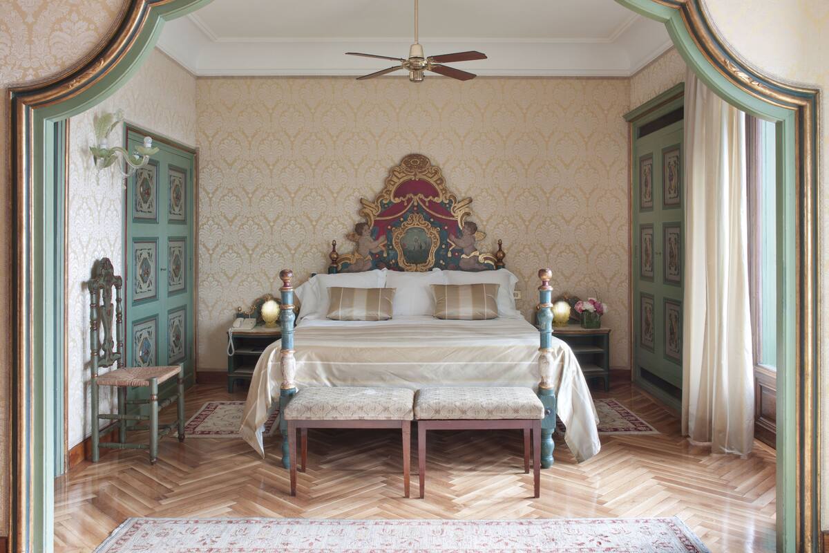 Ein Schlafzimmer mit einem großen Bett, einem Deckenventilator, einem verzierten Kopfteil und einem spiegeln, der in einem grünen Rahmen ist.