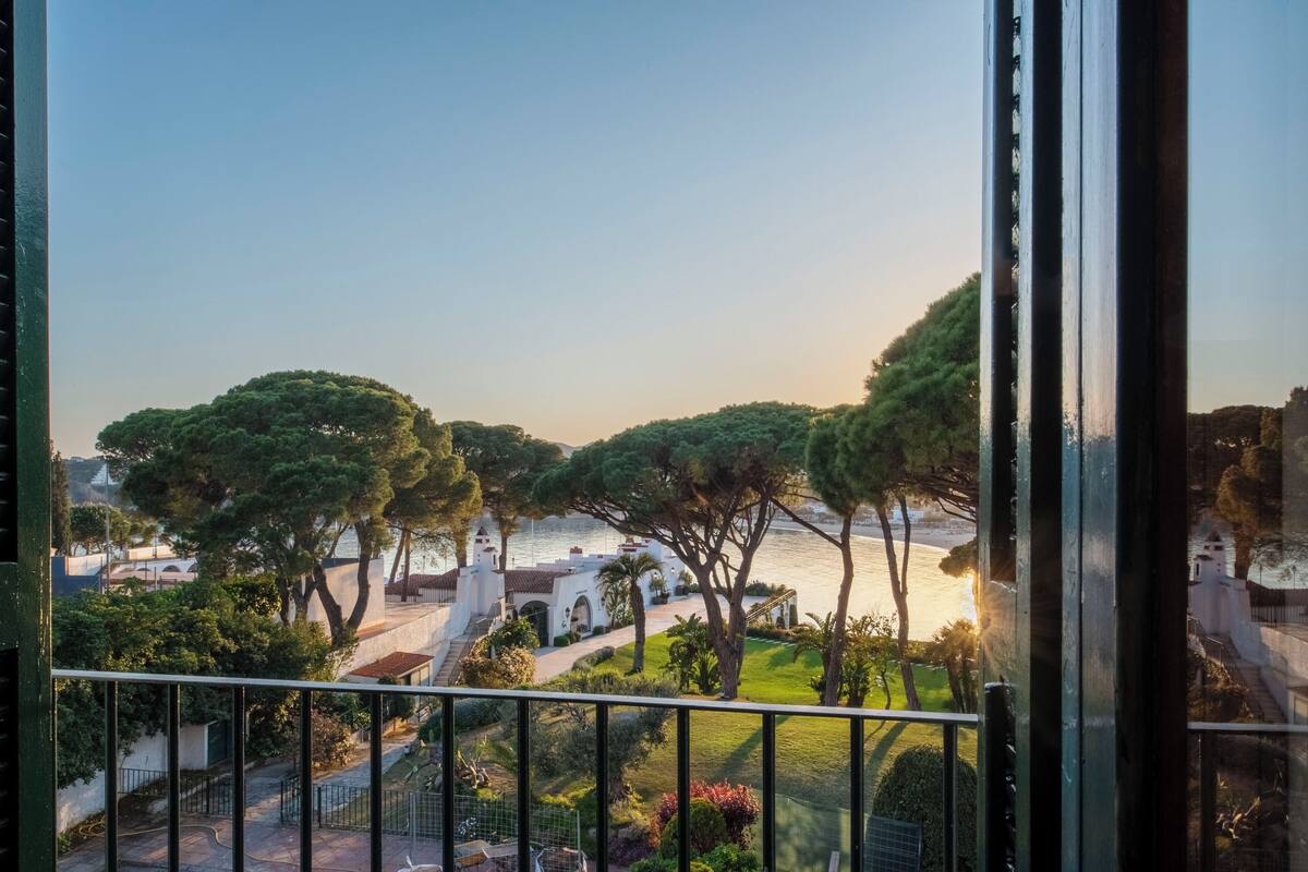 Ein Balkon mit Blick auf eine Küstenlandschaft, darunter Bäume und ein Gebäude mit Bögen.