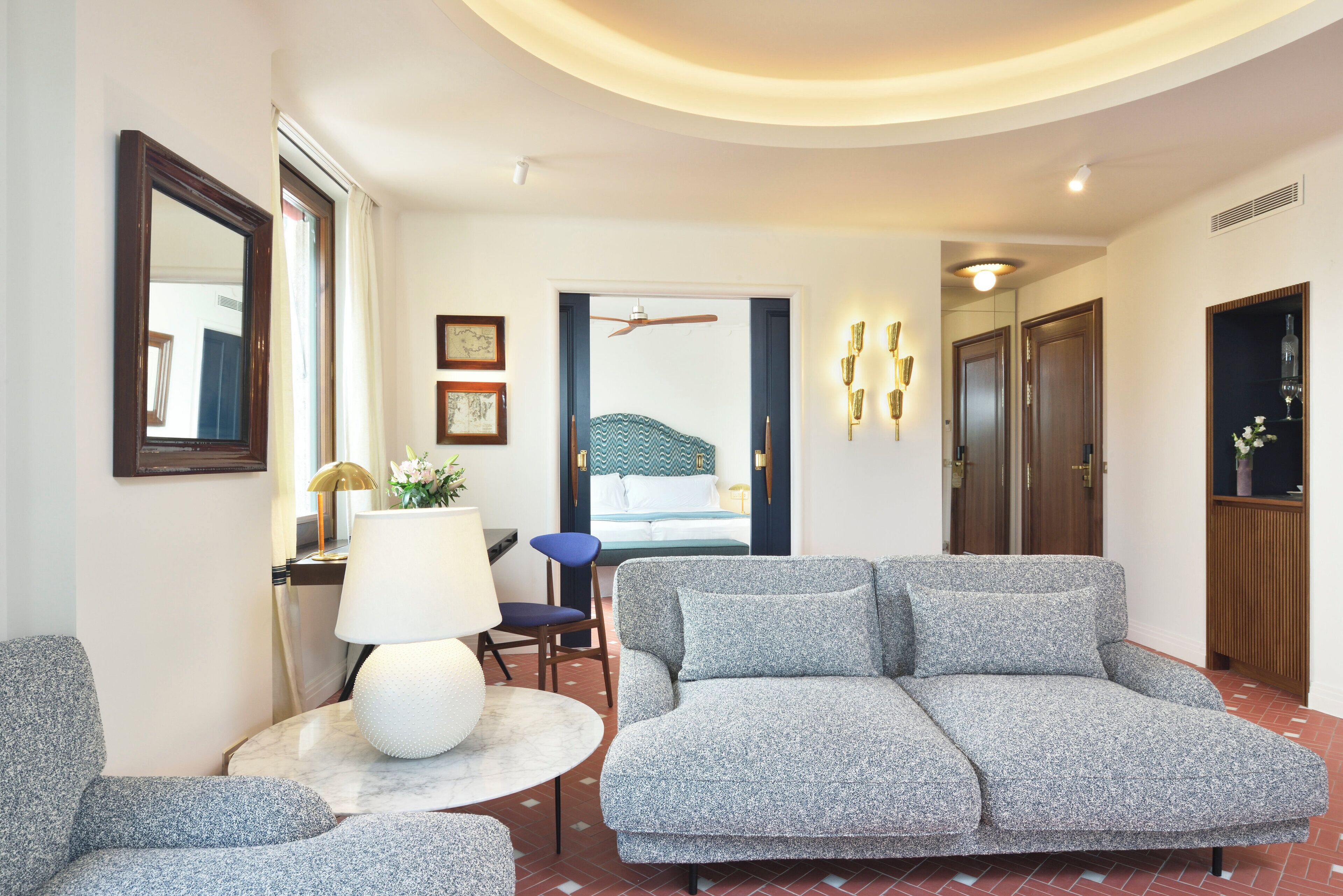 Una sala moderna con un sofá gris, una mesa redonda con una lámpara y una silla azul.