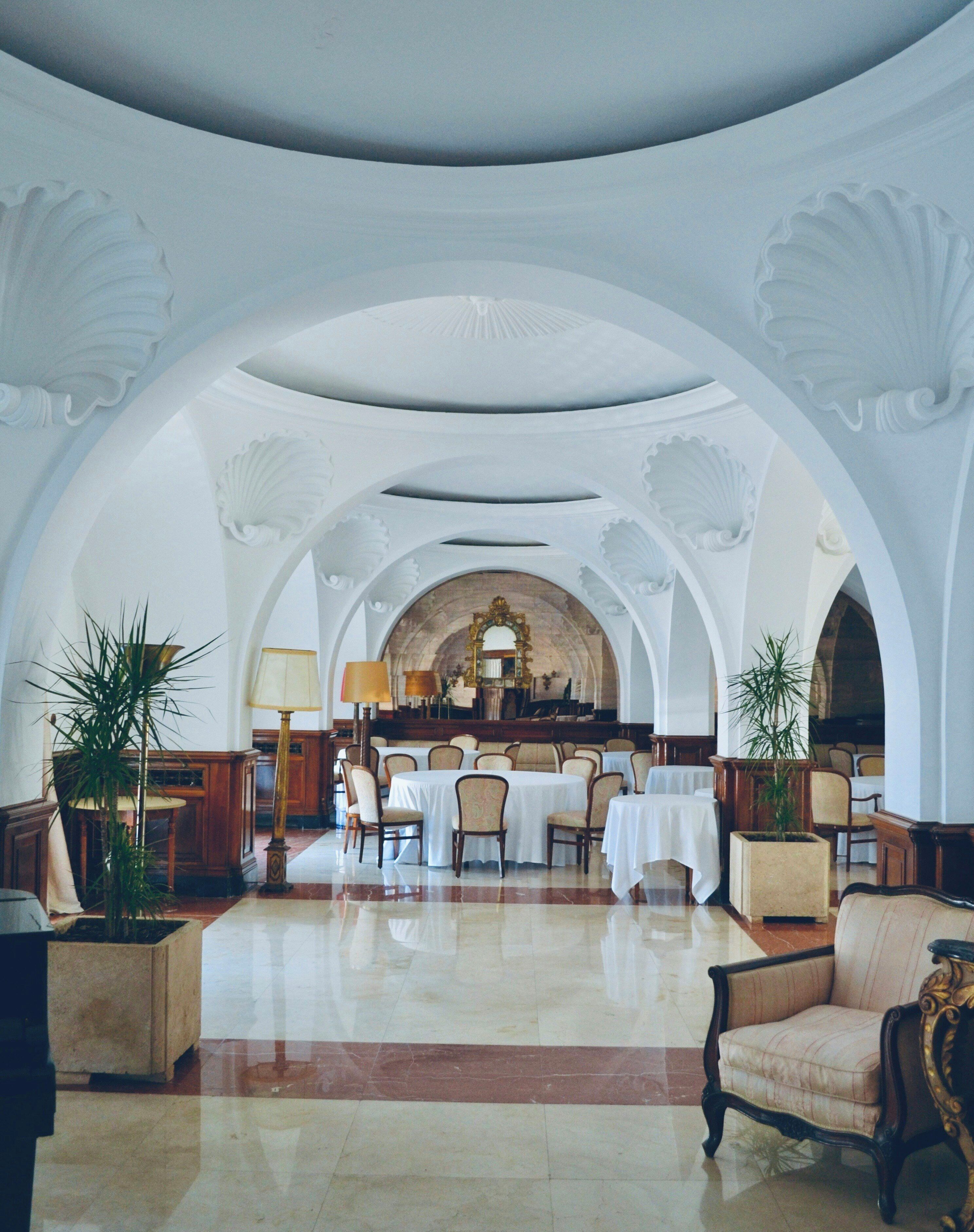 A spacious lobby with a high ceiling, arched ceilings, and a central dining area with tables and chairs.