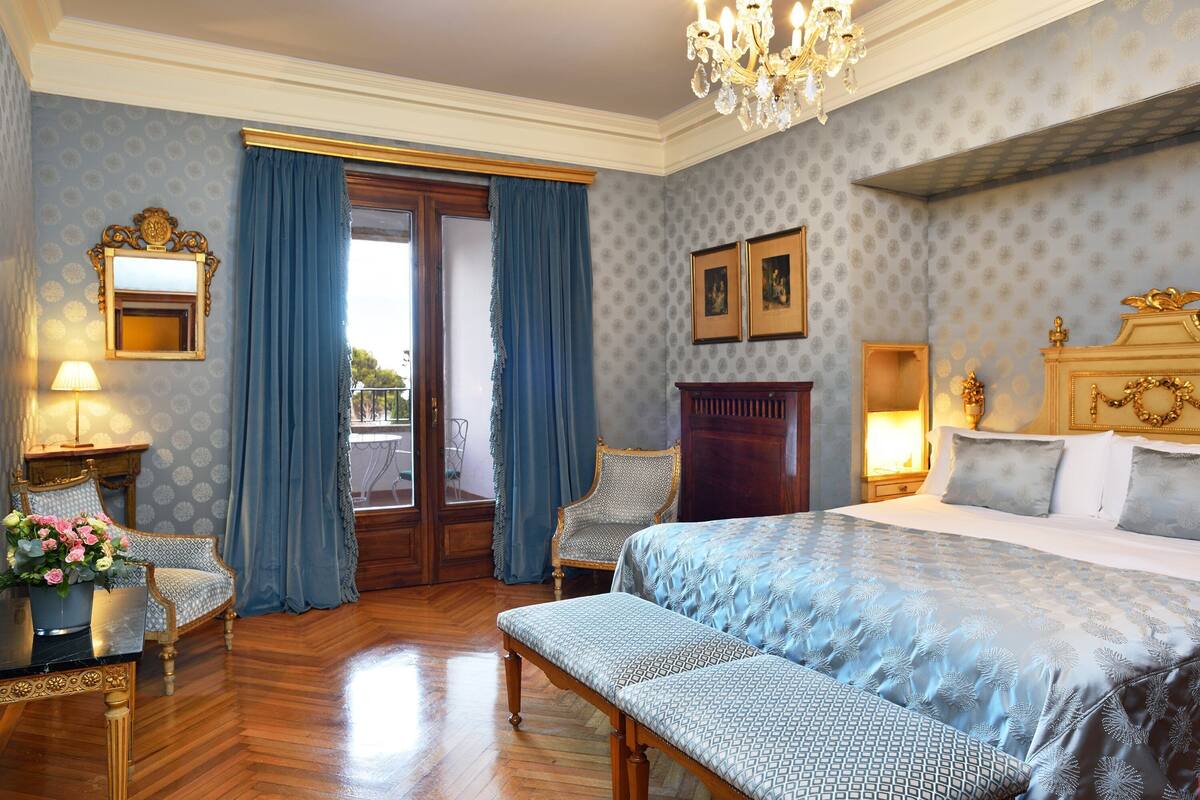 Ein Schlafzimmer mit einem großen Bett, einer Bank, einem Sessel, einem Schminktisch und einer Chandelier.