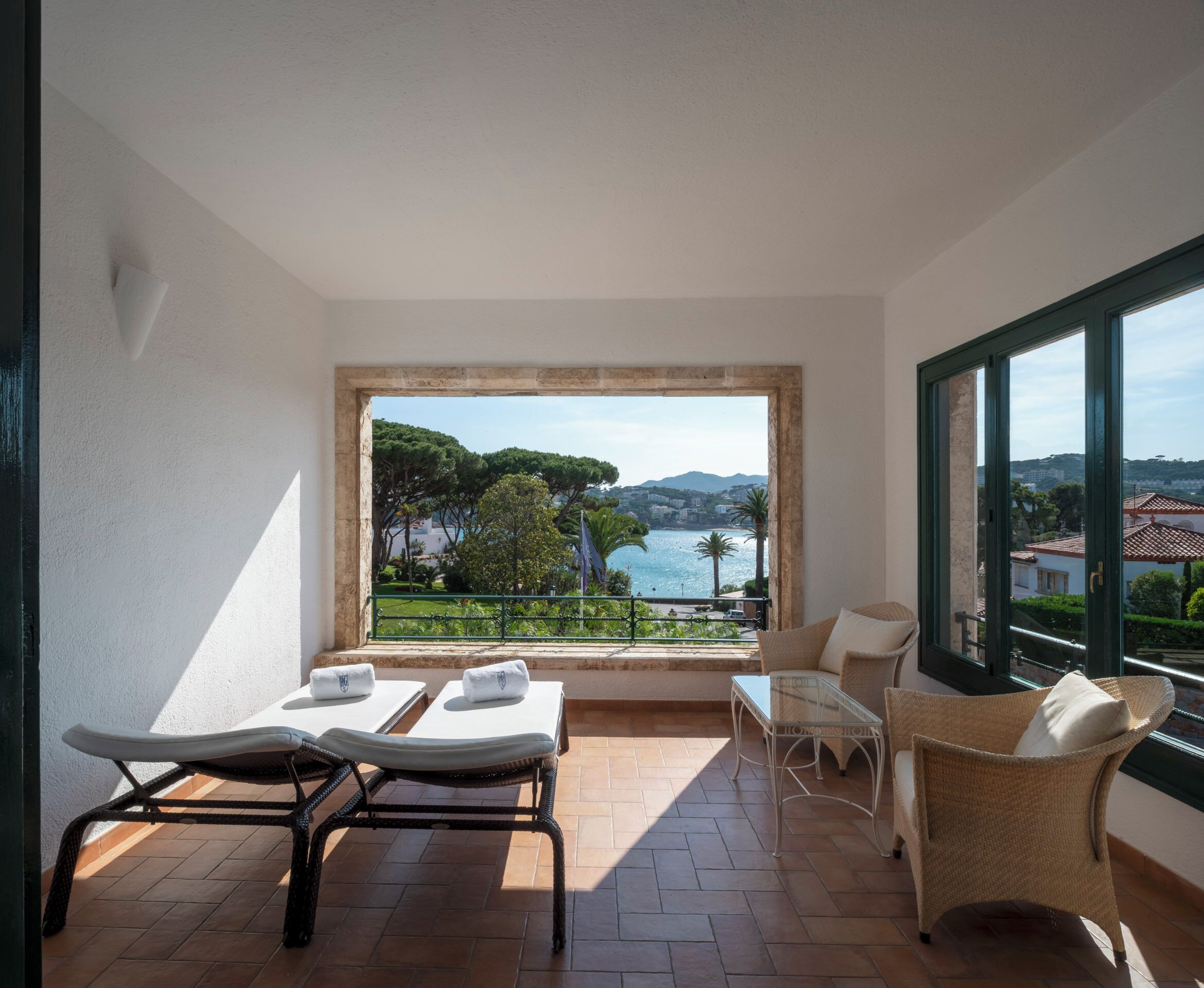 A balcony with two sun loungers, a wicker chair, and a small table.