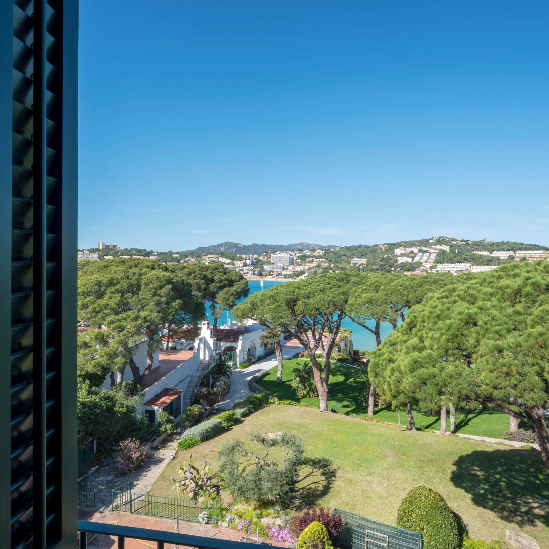 A coastal view with a clear sky, a grassy area with trees, and a distant cityscape.
