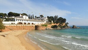 A coastal hotel with a beach view, stone walls, and flags.