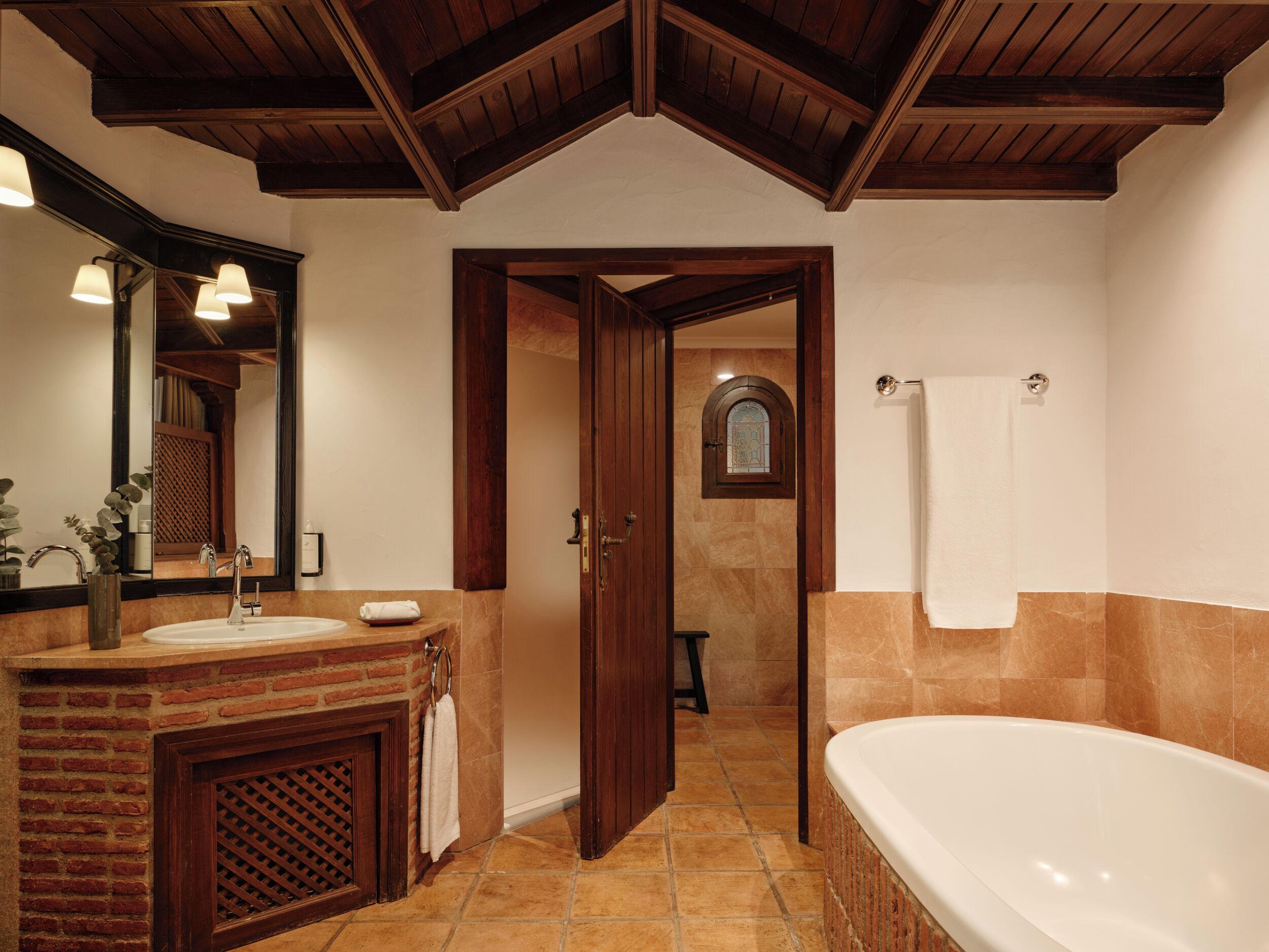 Une salle de bain avec une baignoire, un lavabo, un miroir et une porte donnant sur une autre pièce.