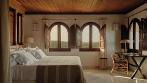 A bedroom with a bed, a desk, and two windows with curtains. - Finca la Bobadilla, Leading Hotels of the World (Loja)