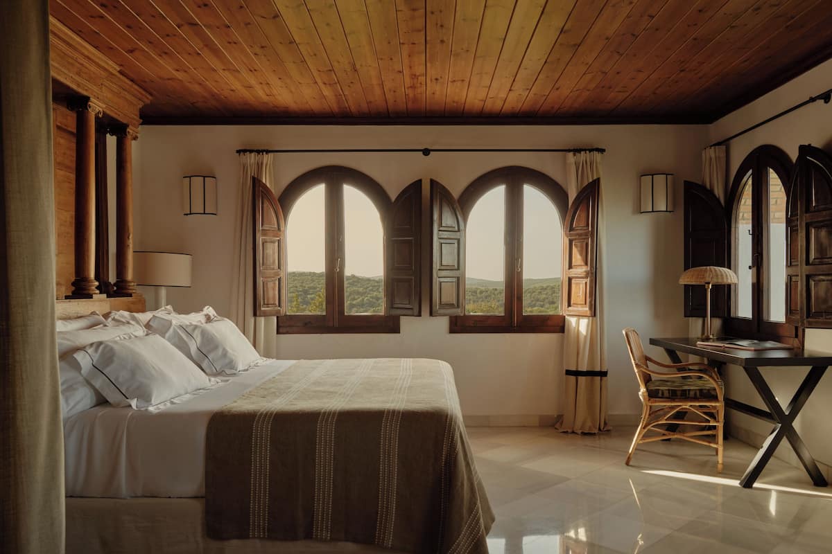 Une chambre à coucher avec un lit, un bureau et deux fenêtres avec des rideaux.