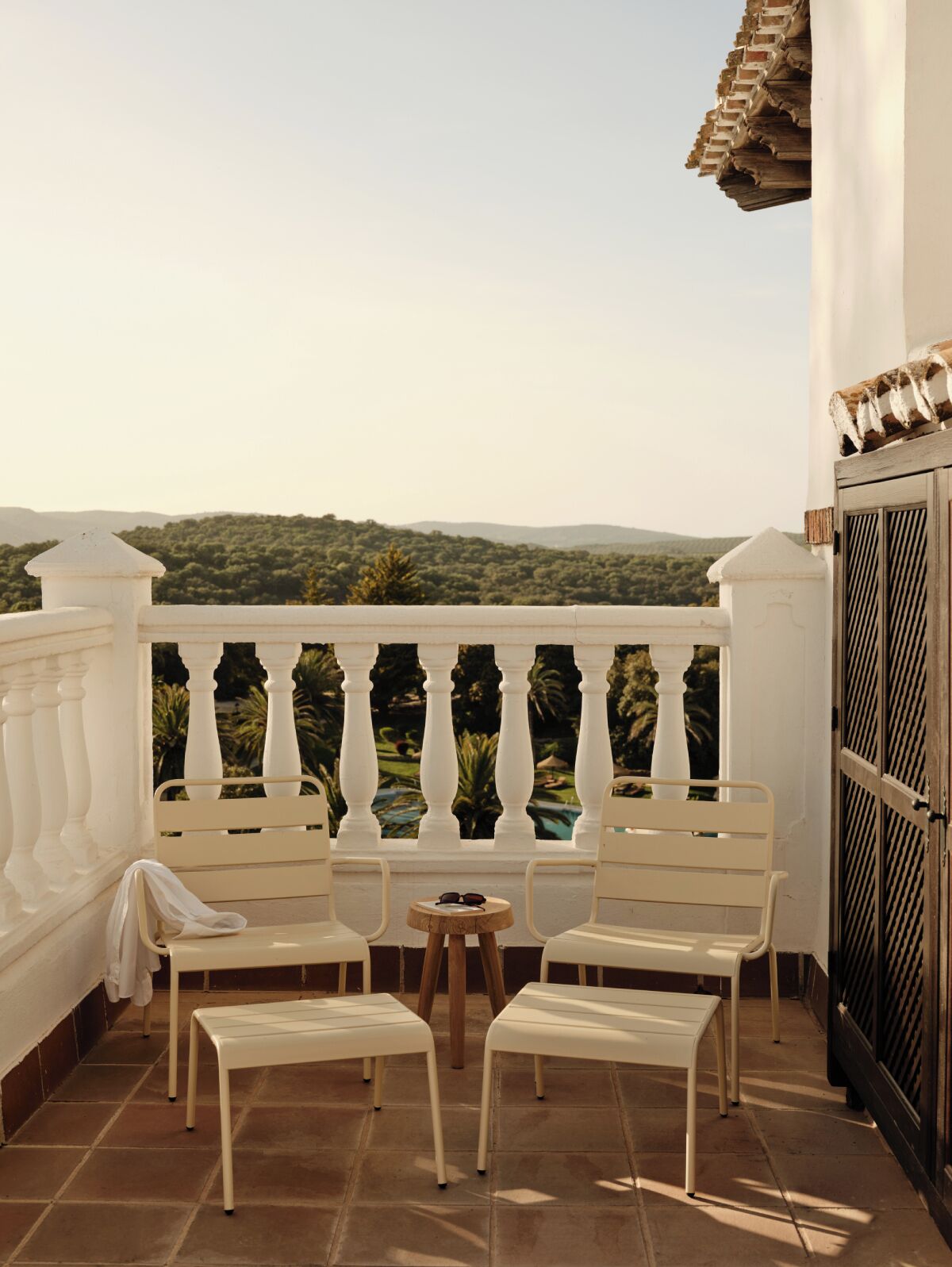 A balcony with white chairs and a small round table, overlooking a lush green landscape.