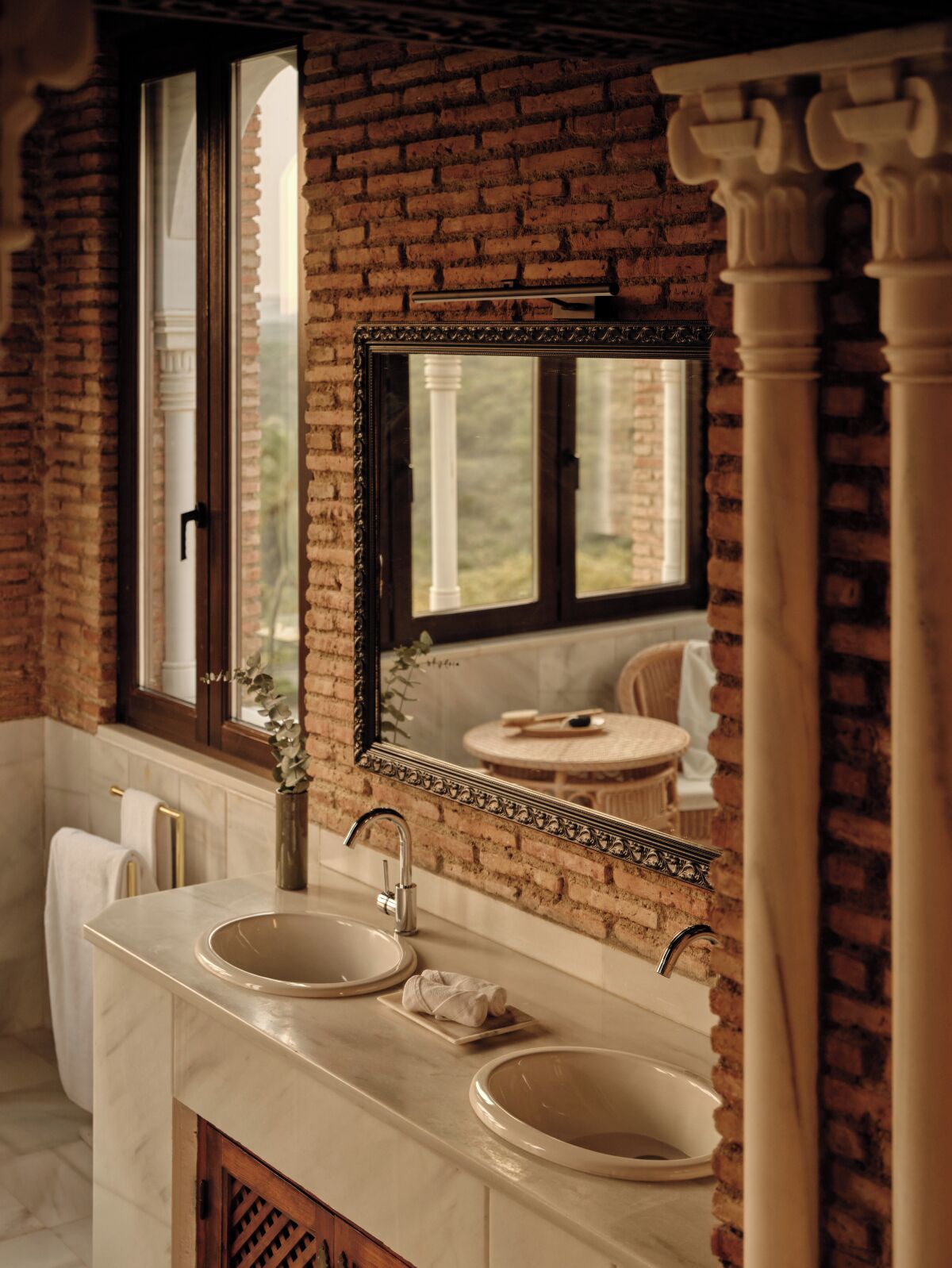 Un baño con lavamanos doble, un espejo grande y vista a un jardín a través de una ventana.