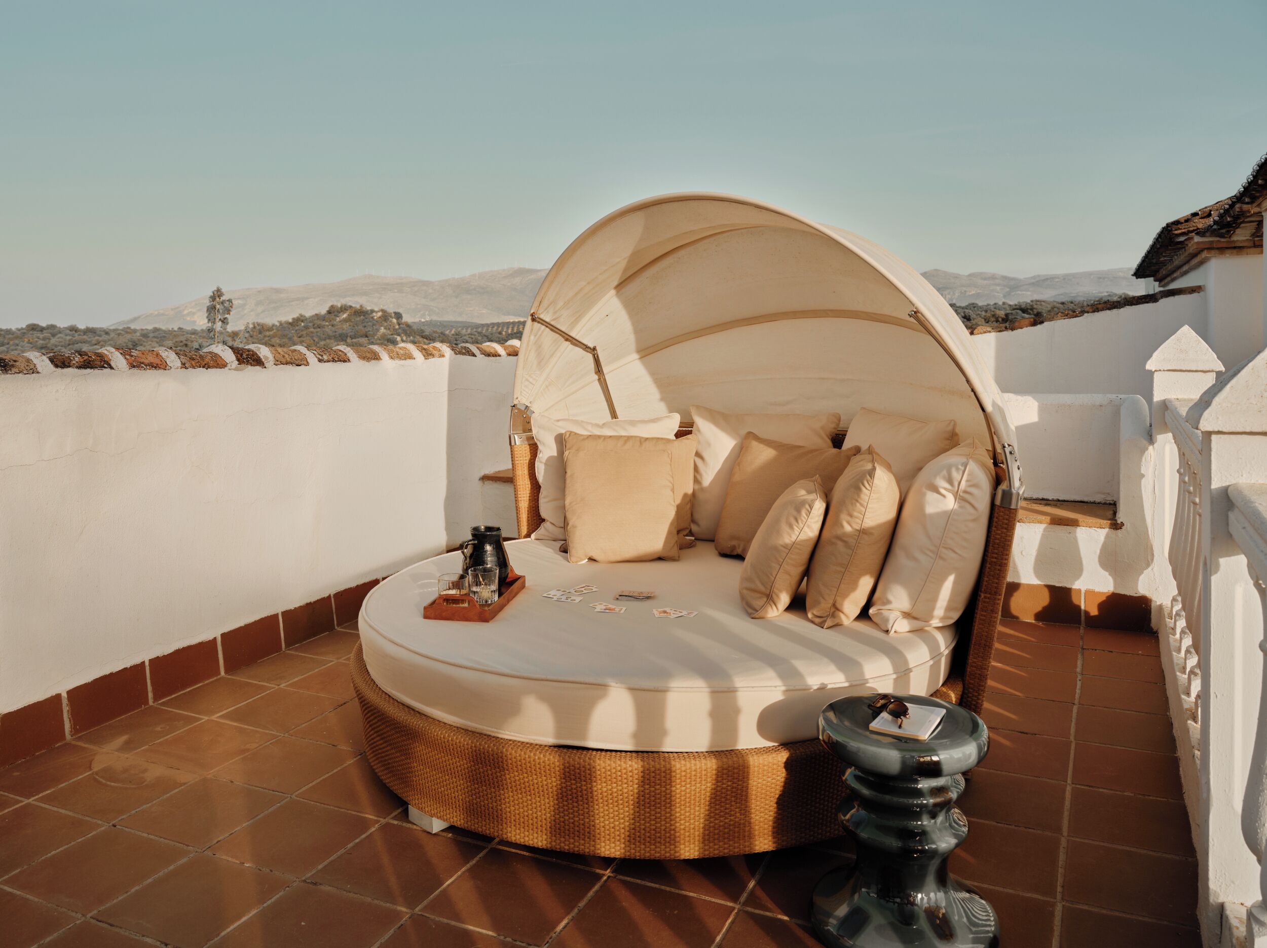 Una cama redonda con dosel en una terraza en la azotea con vistas a colinas distantes.