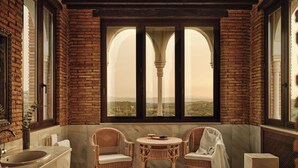 A room with a brick wall, a large arched window, a round table, two wicker chairs, and a marble sink. - Finca la Bobadilla, Leading Hotels of the World (Loja)