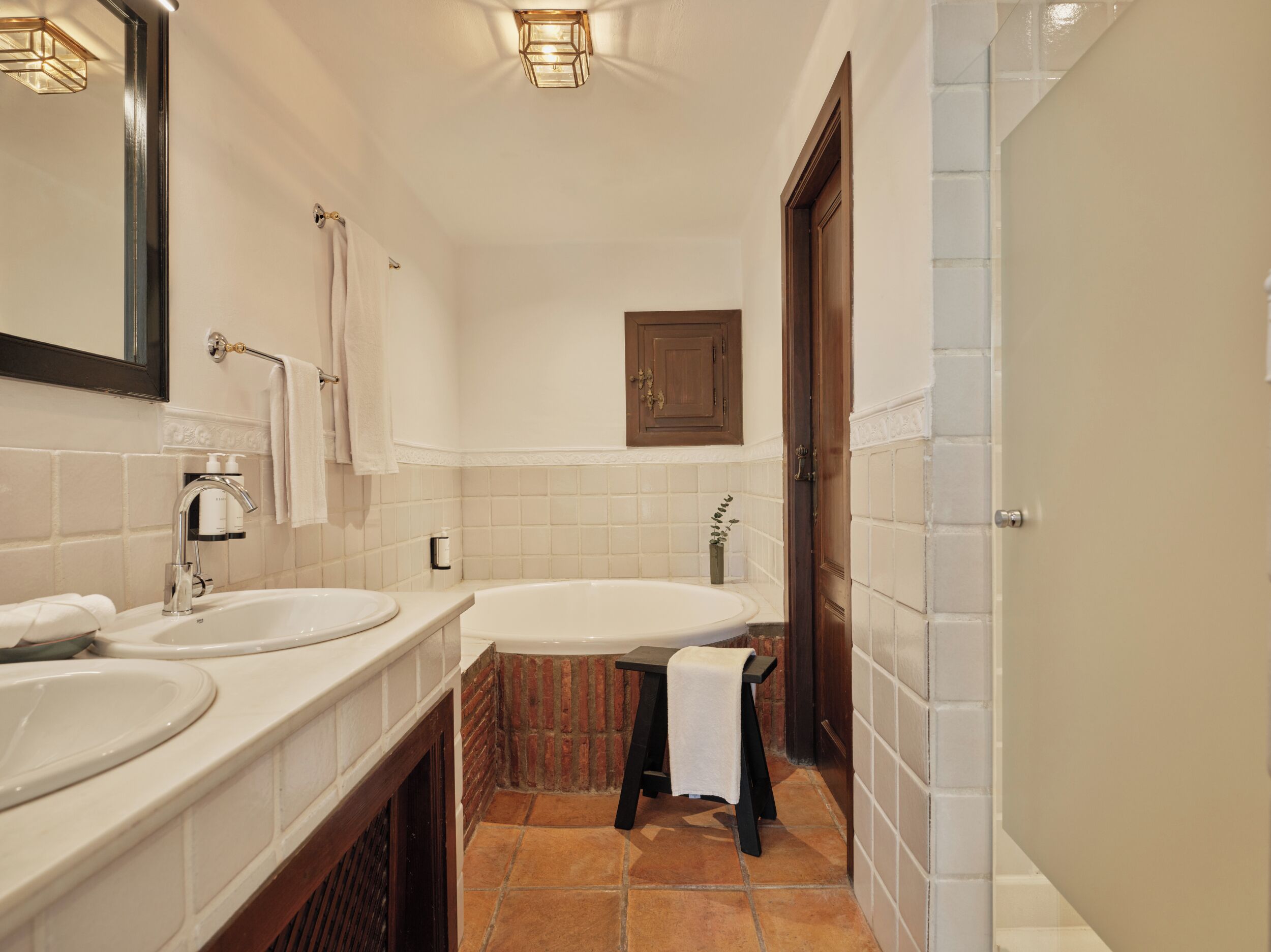 A bathroom with two sinks, a bathtub, a mirror, a towel rack, and a door.