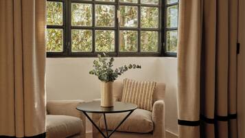 Una habitación con ventana, una pequeña mesa con un florero y dos sillones.