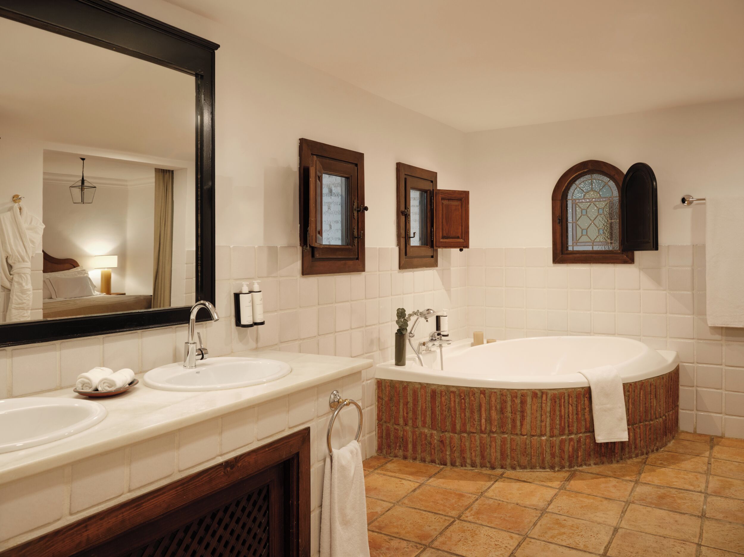 A bathroom with two sinks, a large bathtub, a mirror, and a window with a stained glass design.