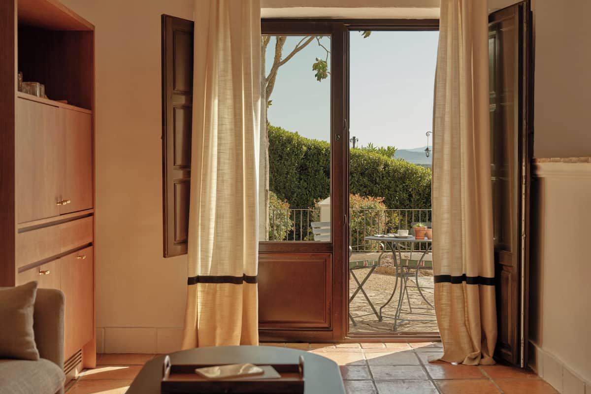 Une chambre comprenant un lit, une armoire en bois et une porte-fenêtre coulissante donnant sur une terrasse extérieure avec une table et des chaises.