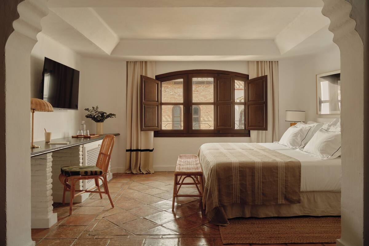 Une chambre à coucher avec un lit, un bureau, une chaise, une fenêtre et un téléviseur.